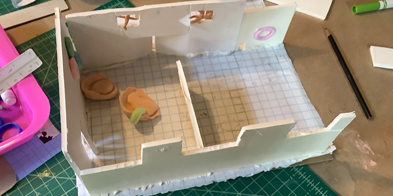A two-room model created by a summer camp participant is displayed on a drafting table