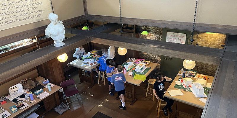 A view from the Drafting Room balcony shows the model-building process in full swing as campers craft and collaborate.